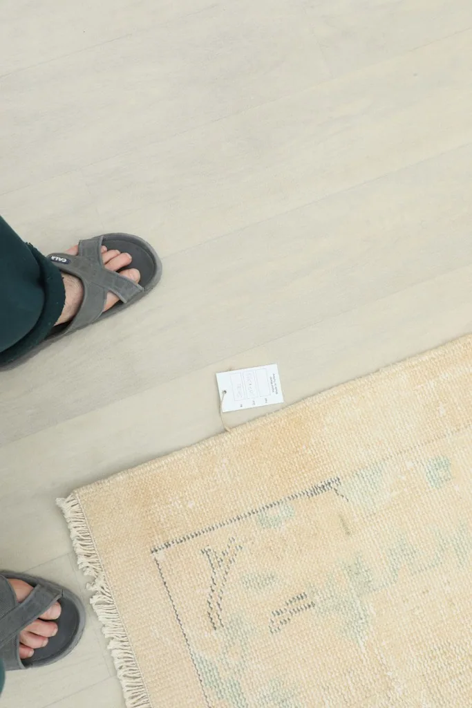 Overhead view of a person's feet next to the rug, indicating scale and the rug's texture.