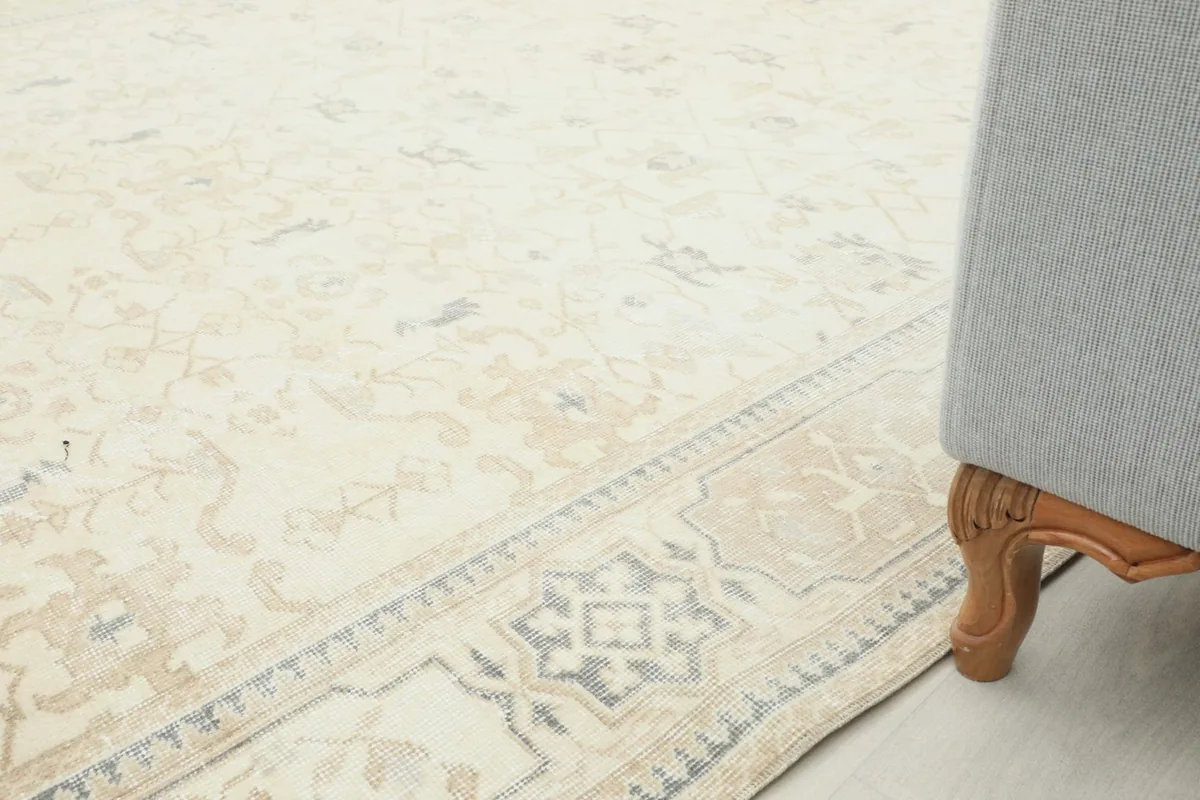 Side view of the rug's border next to furniture, showing the cream, beige, and gray colors.
