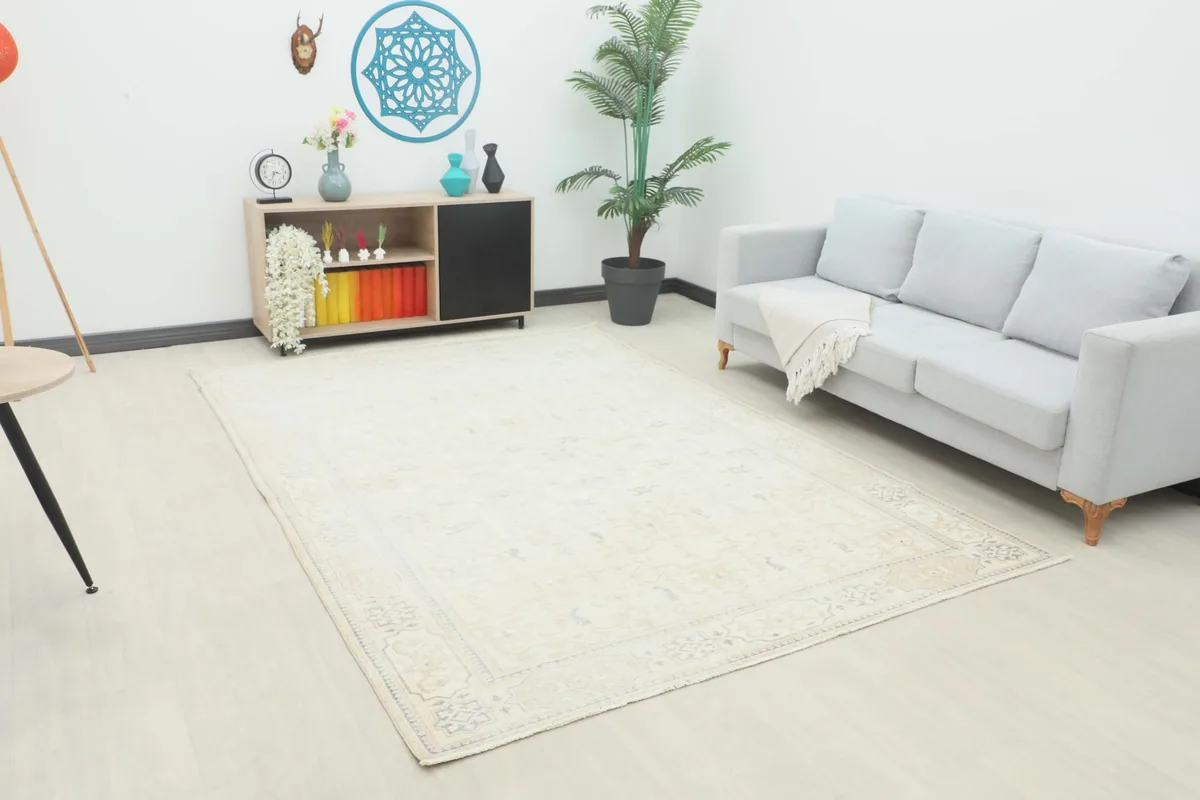 Slightly angled full view of the cream vintage rug in a room setting with a couch.