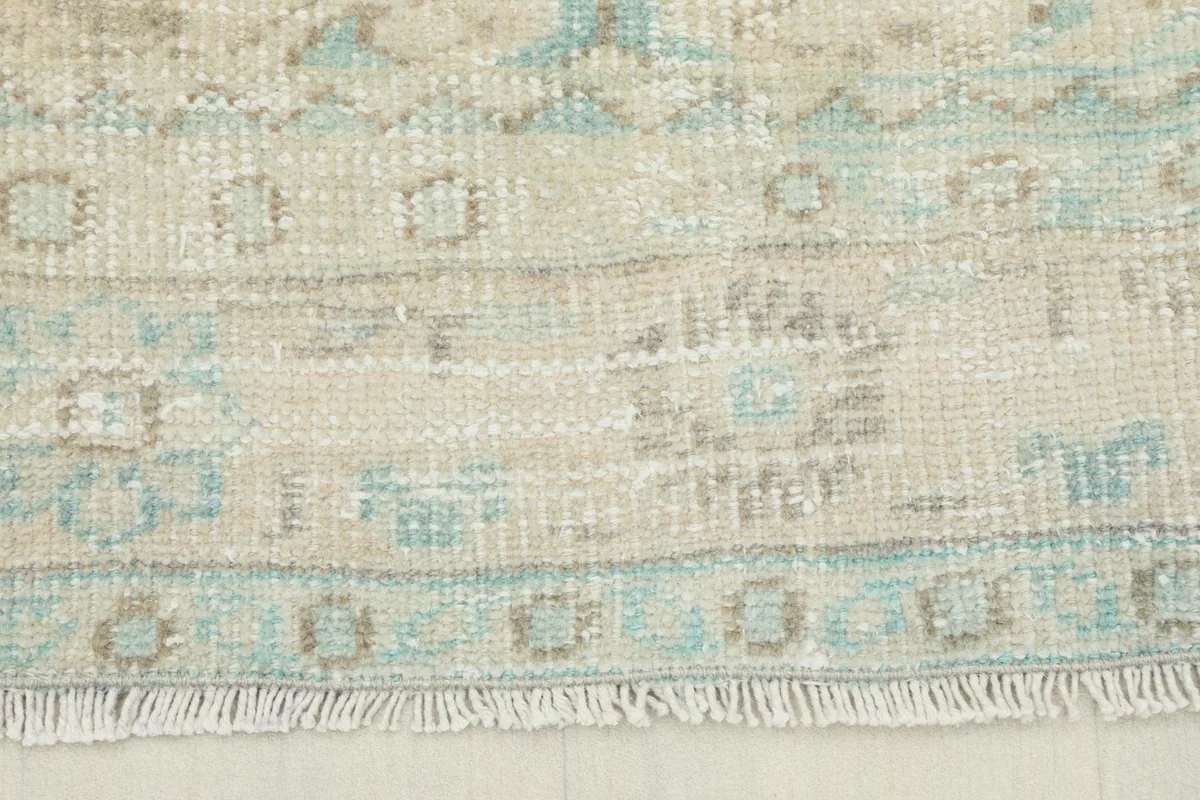Close-up detail of the fringe and faded geometric border pattern in beige and blue