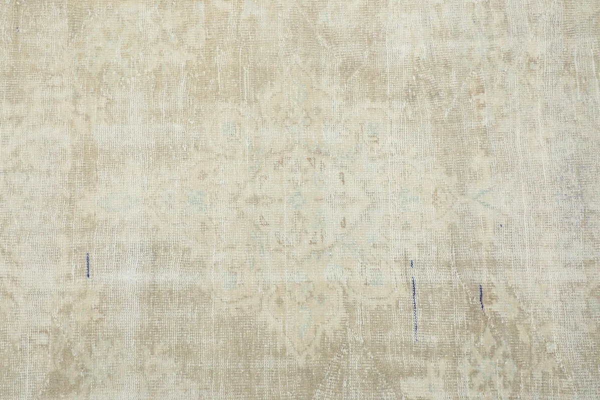 Straight overhead view of the central field of the rug, showing faded patterns and variations in beige