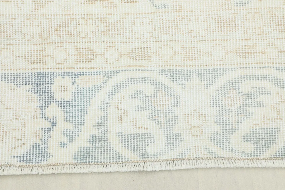 Close-up view of the rug's border showing faded blue and beige patterns and low pile.