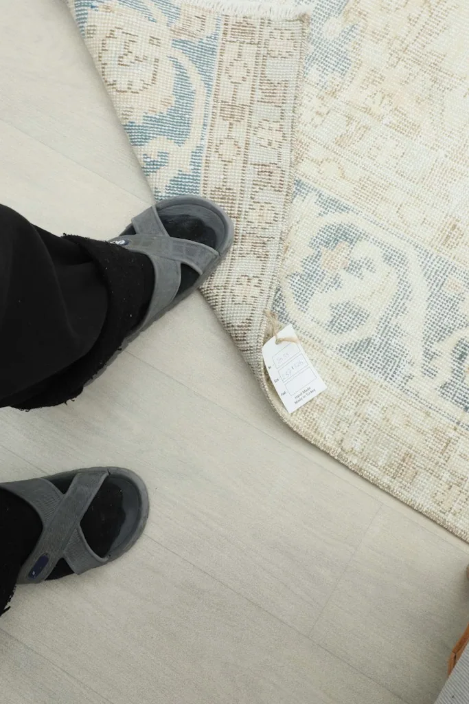 Person's feet next to the rug, indicating its scale and showing a product tag.