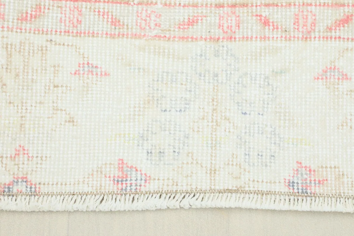Close-up detail of the fringe and a section of the beige border and faded rose field.