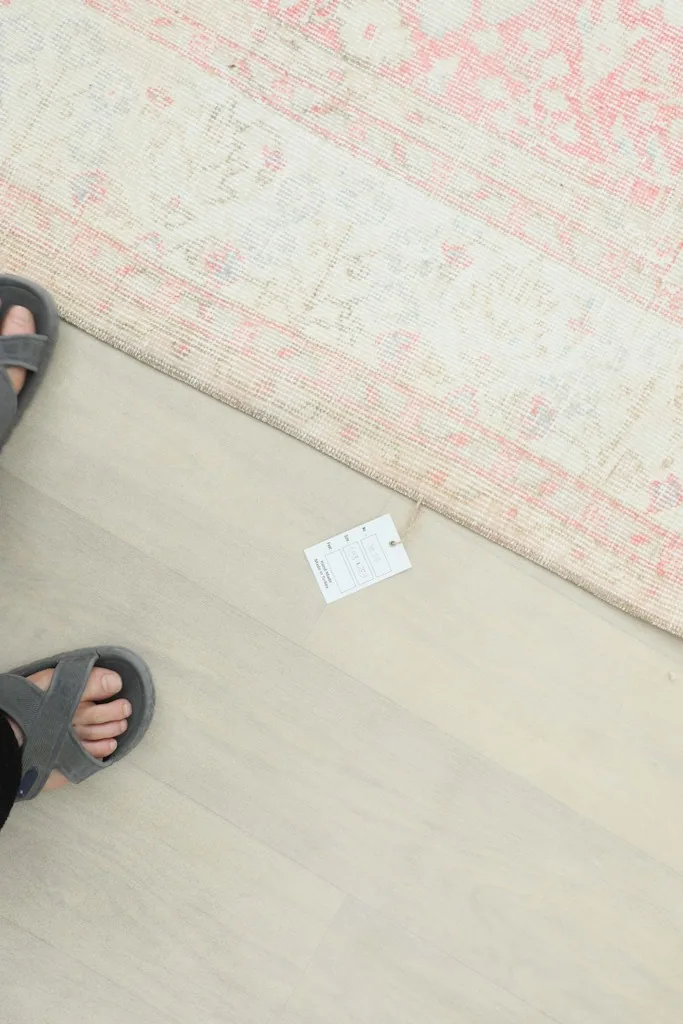 Feet in sandals next to the rug and a size tag, providing a sense of scale.
