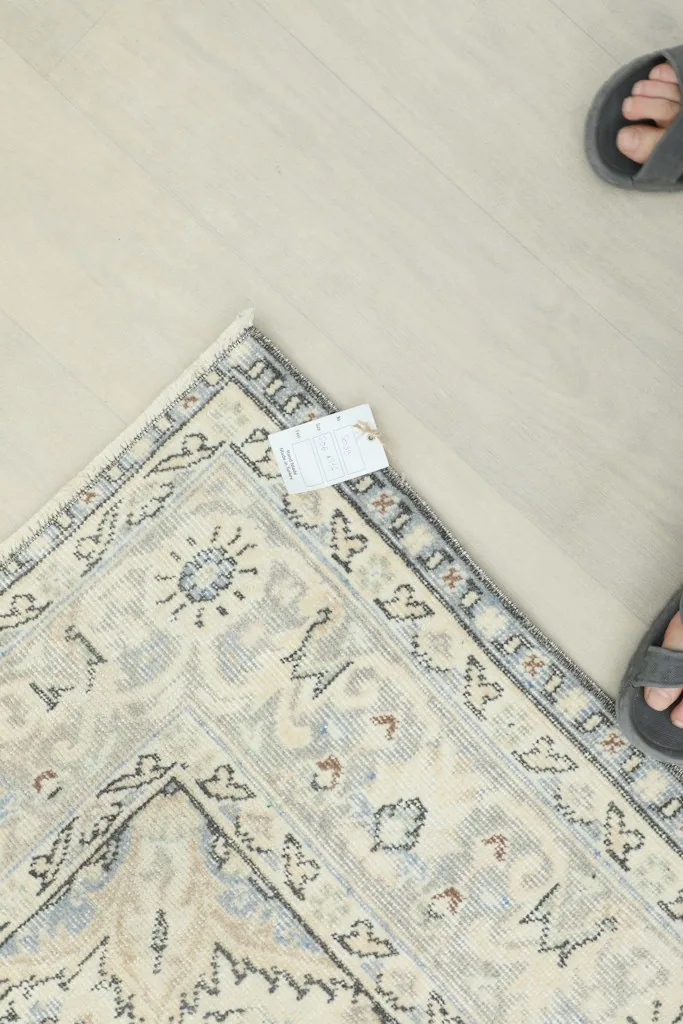 Overhead detail of the rug's fringe and a small tag, with feet in sandals on the floor.