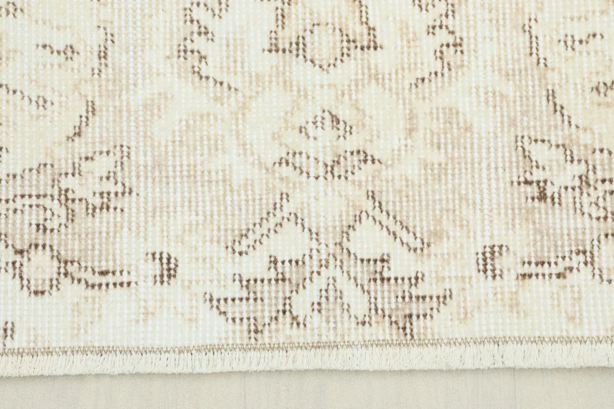 Close-up of the rug's border showing a geometric pattern and the soft ivory and beige colors.