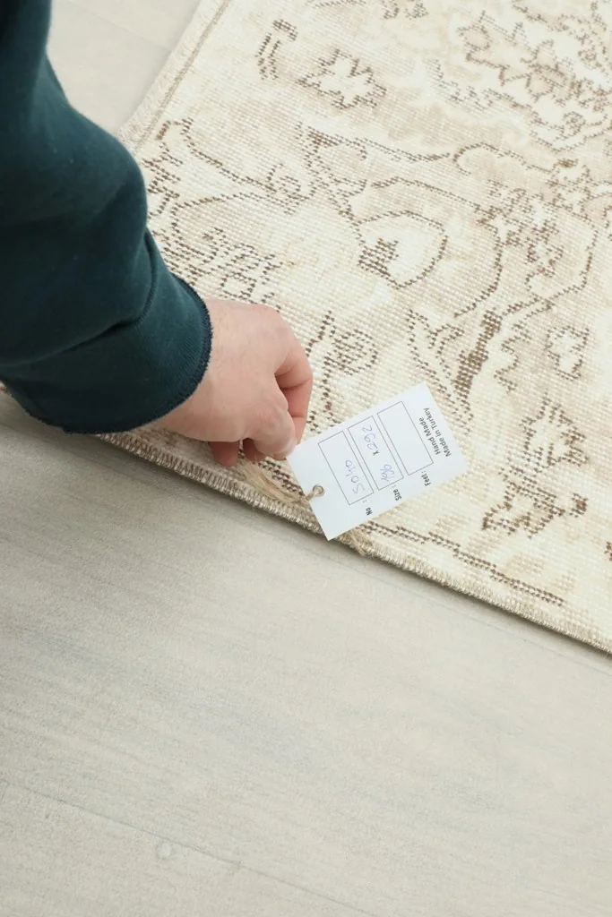 Hand holding a measurement tag near the rug's edge, indicating its dimensions and characteristics.