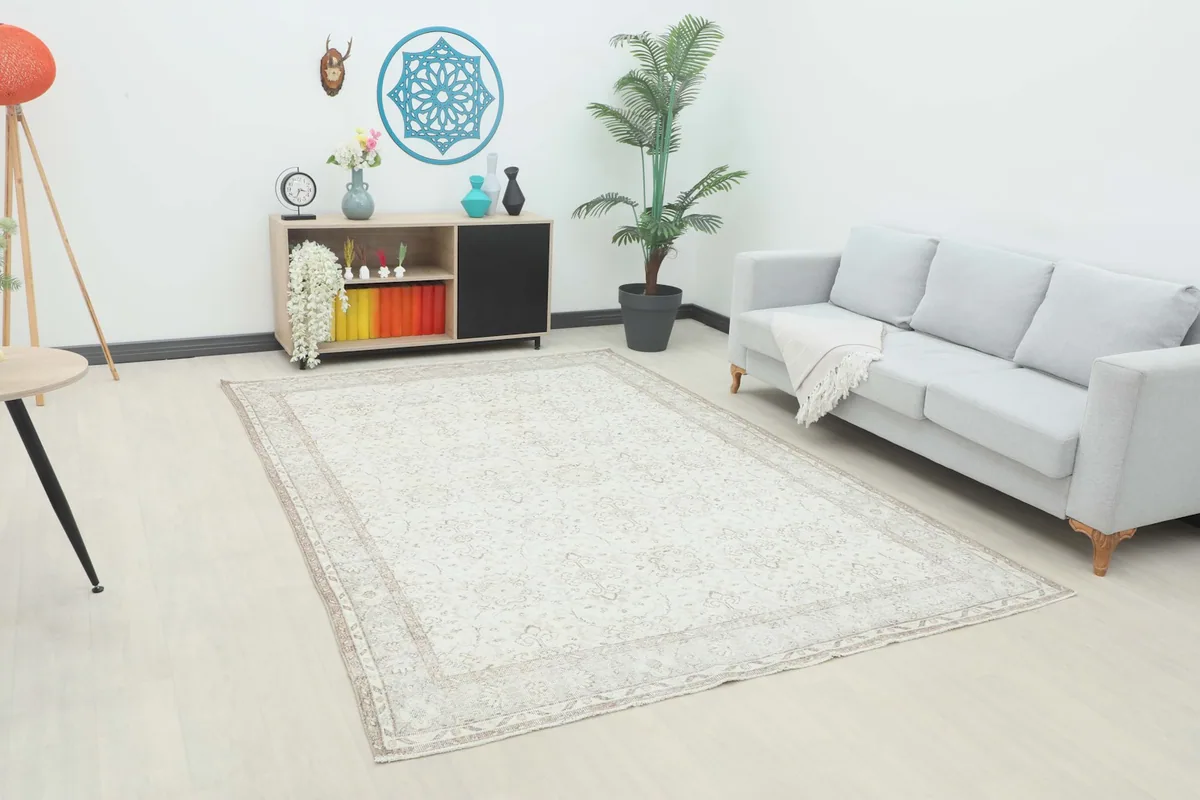 Ivory beige vintage rug displayed in a room setting with a light gray sofa and wooden cabinet.