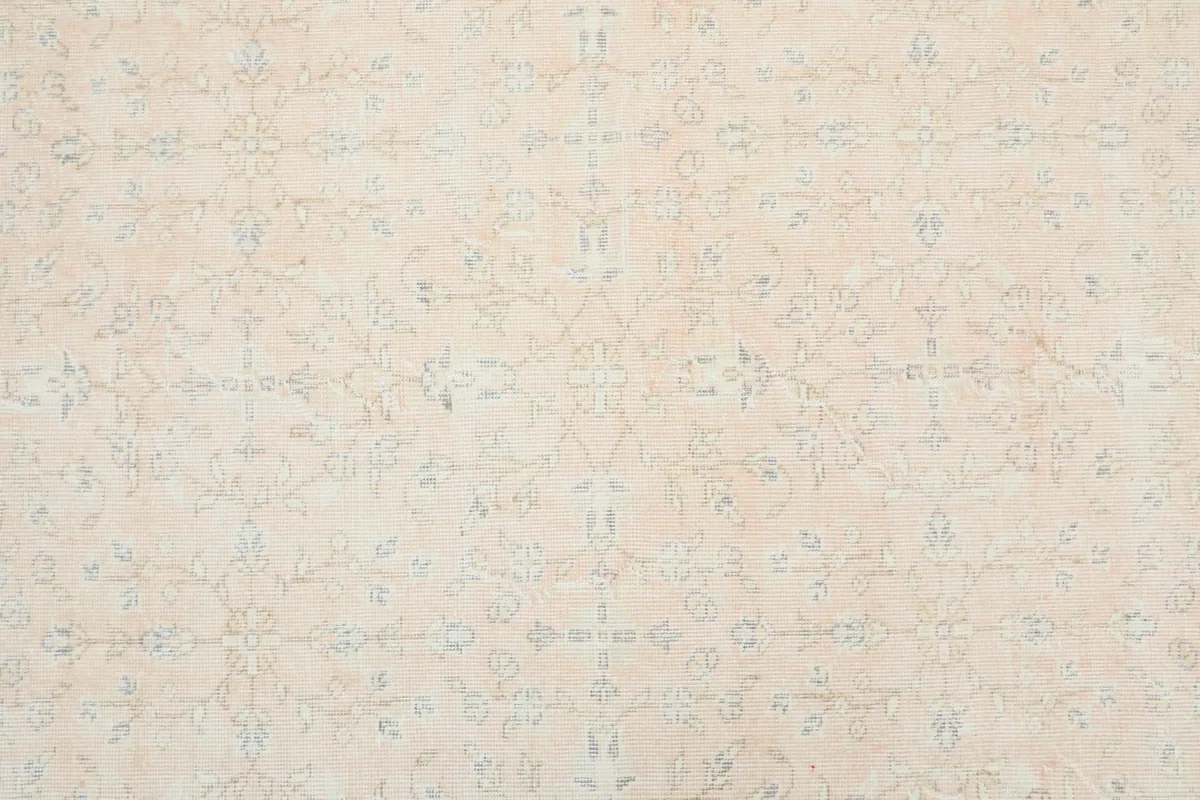 Detailed overhead view of the rug's central field showcasing faded floral and geometric patterns in beige and light blue