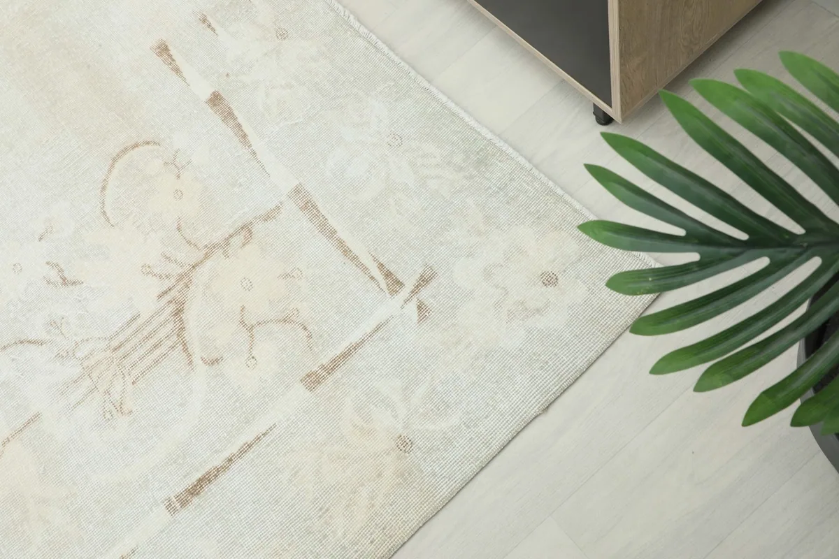 Angled view of the vintage rug's surface and faded patterns, next to a green plant.