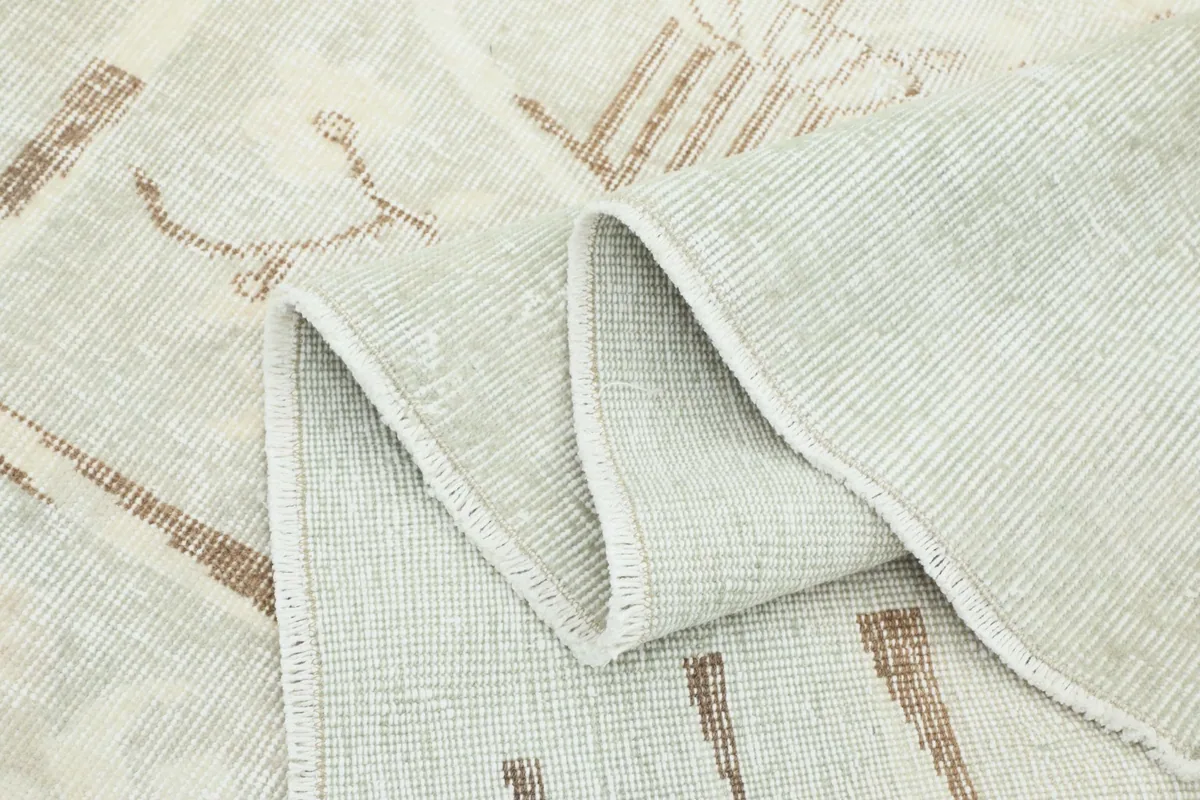 Folded rug showing the reverse side with the cotton foundation and the front with faded patterns.