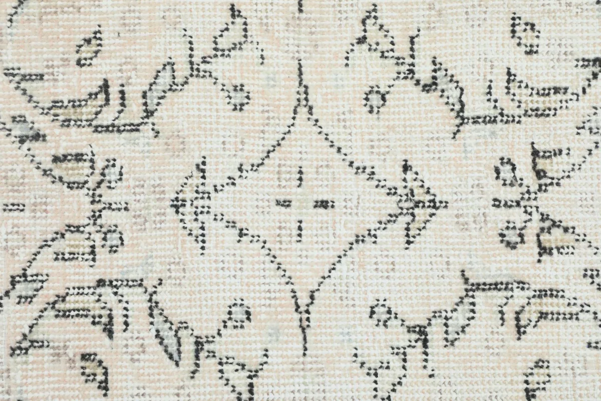 Detailed view of the low wool pile and the intricate charcoal motifs on the ivory foundation.