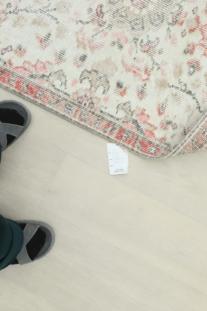 View of the rug's edge and label on the floor, with feet in sandals for scale.