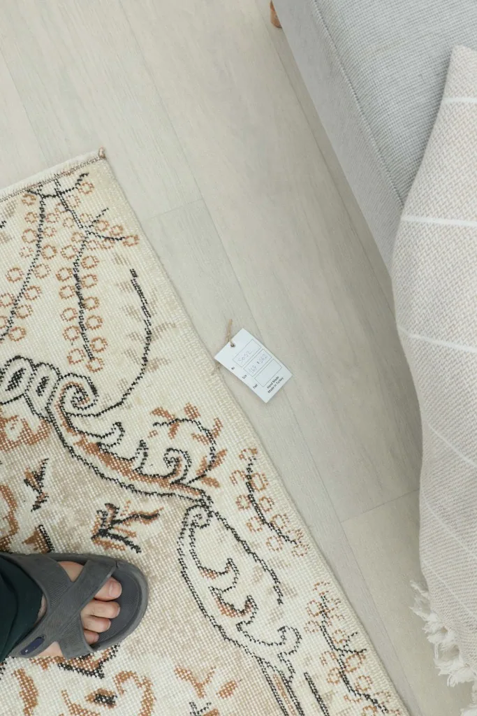 Overhead view of a person's foot next to the rug, showing scale and a product tag