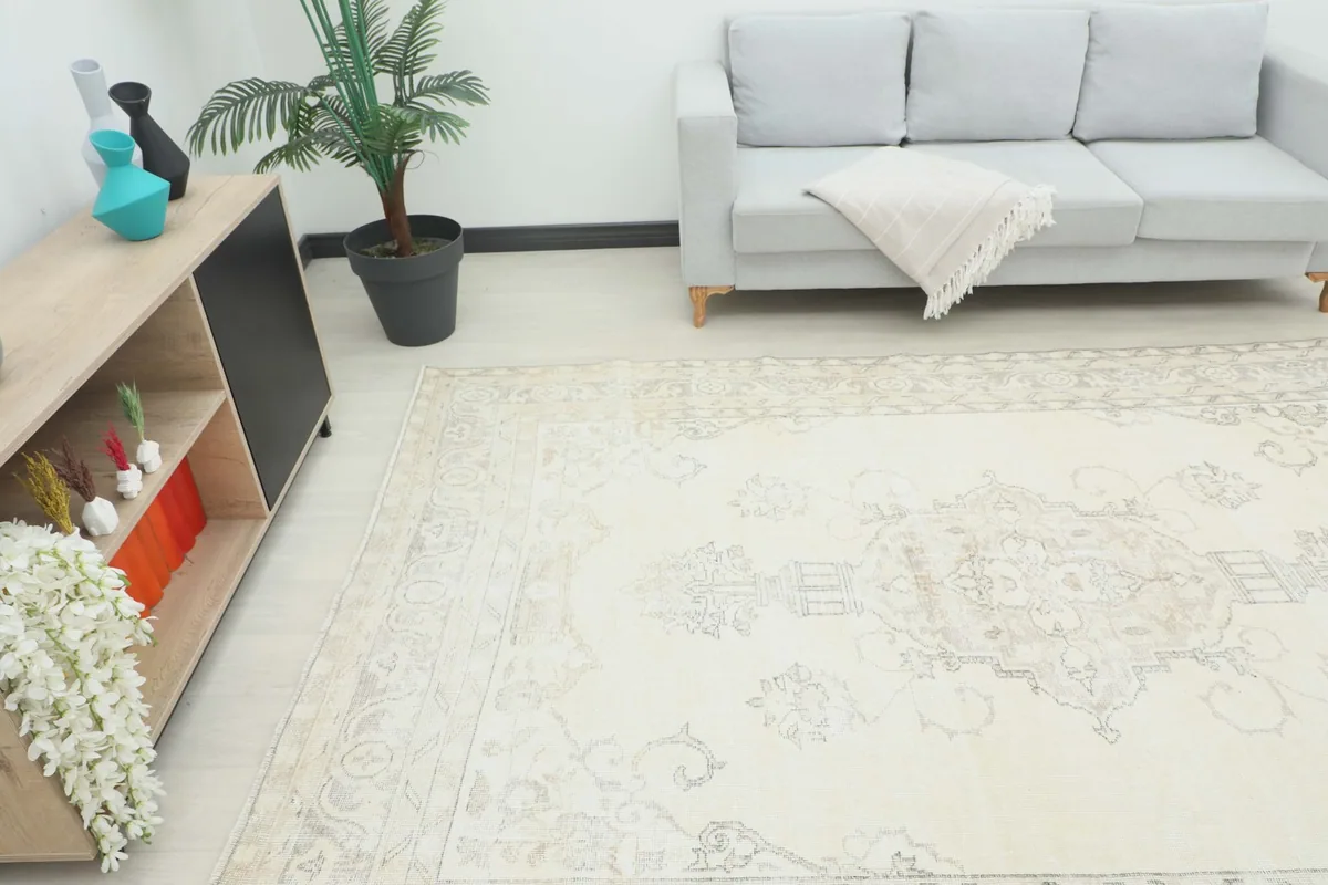 The ivory vintage rug placed in a room with a light gray sofa and modern decor.