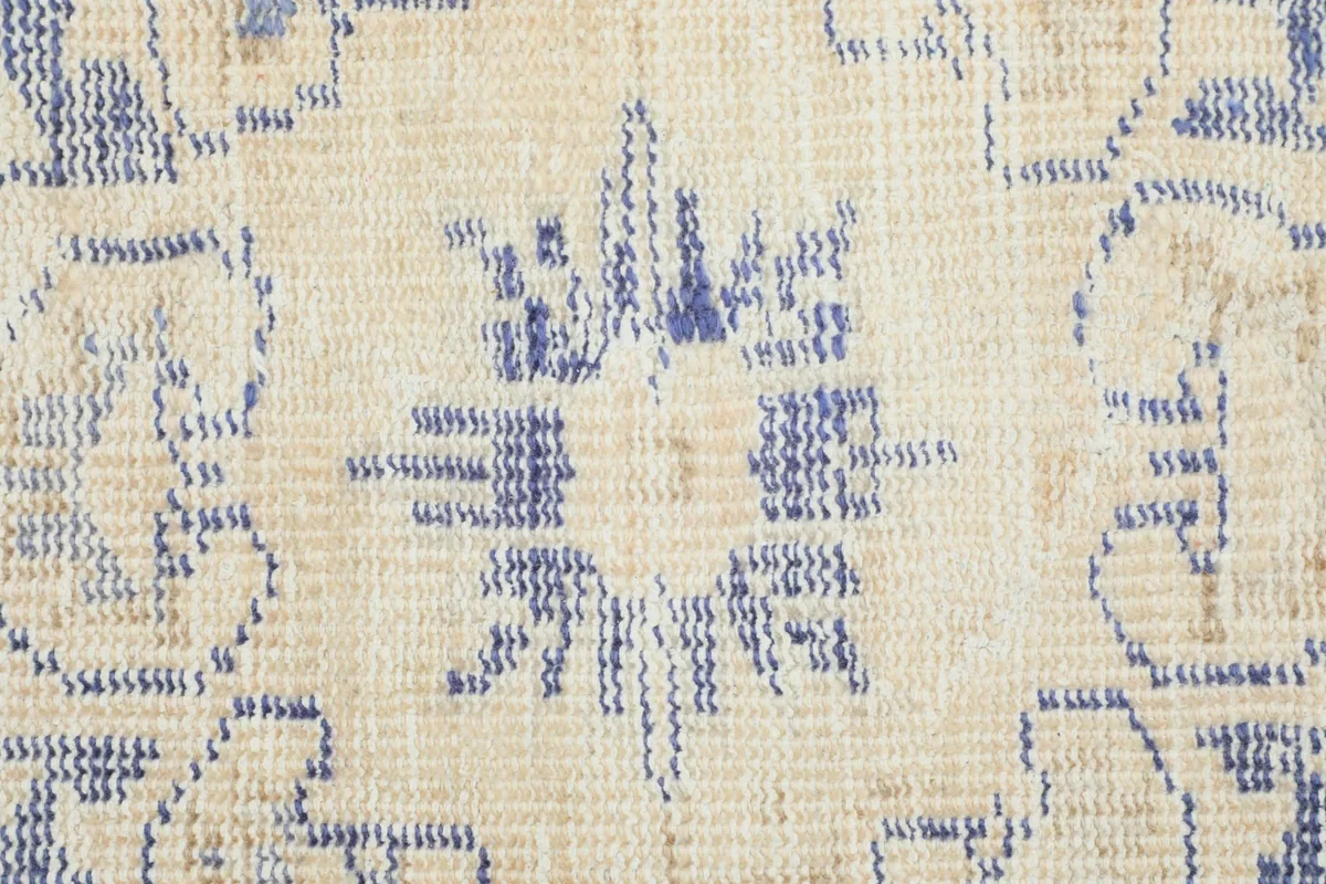 Detailed view of the intricate blue floral and geometric patterns within the beige field of the rug.