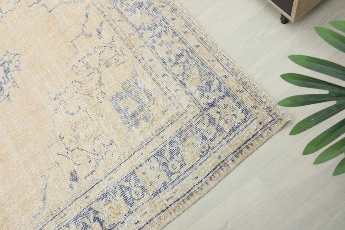 Close-up of the blue border design and corner detail against the beige field of the vintage rug.