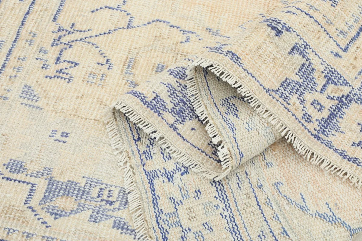 Close-up of the low pile texture and the hand-knotted construction of the beige and blue rug.