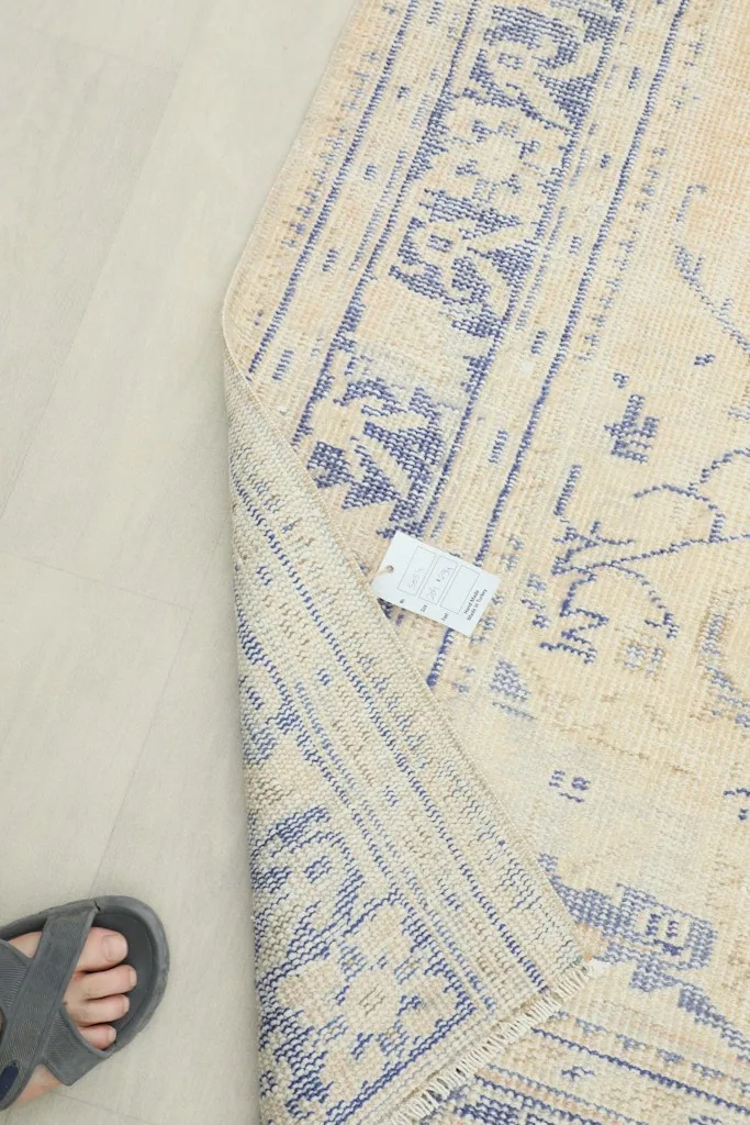 Underside view of the rug, showing the cotton foundation and a small tag, with a foot for scale.