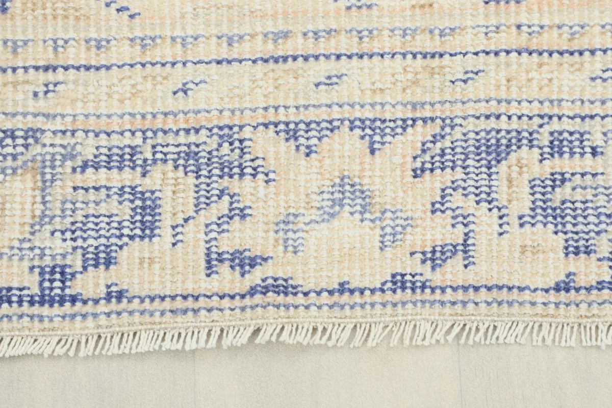 Close-up detail of the fringe and a section of the border pattern on the vintage beige and blue rug.