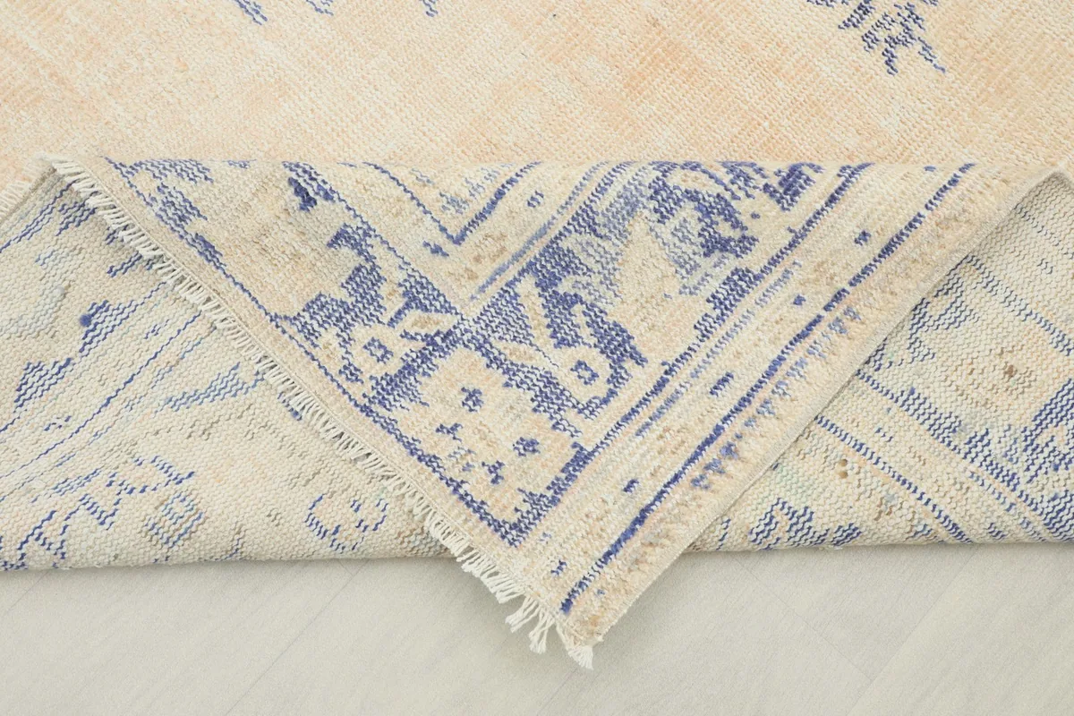 Folded corner of the rug, revealing the wool pile and cotton foundation, with blue and beige colors.