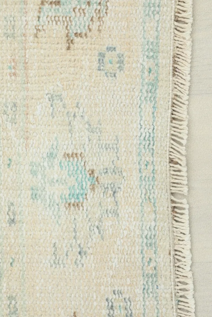 Close-up view of the rug's edge, showing the hand-knotted wool pile, cotton fringe, and subtle blue and brown patterns