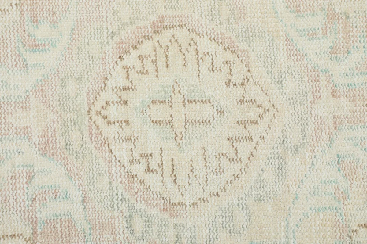 Close-up of a faded geometric motif and texture on the beige wool pile of the hand-knotted rug