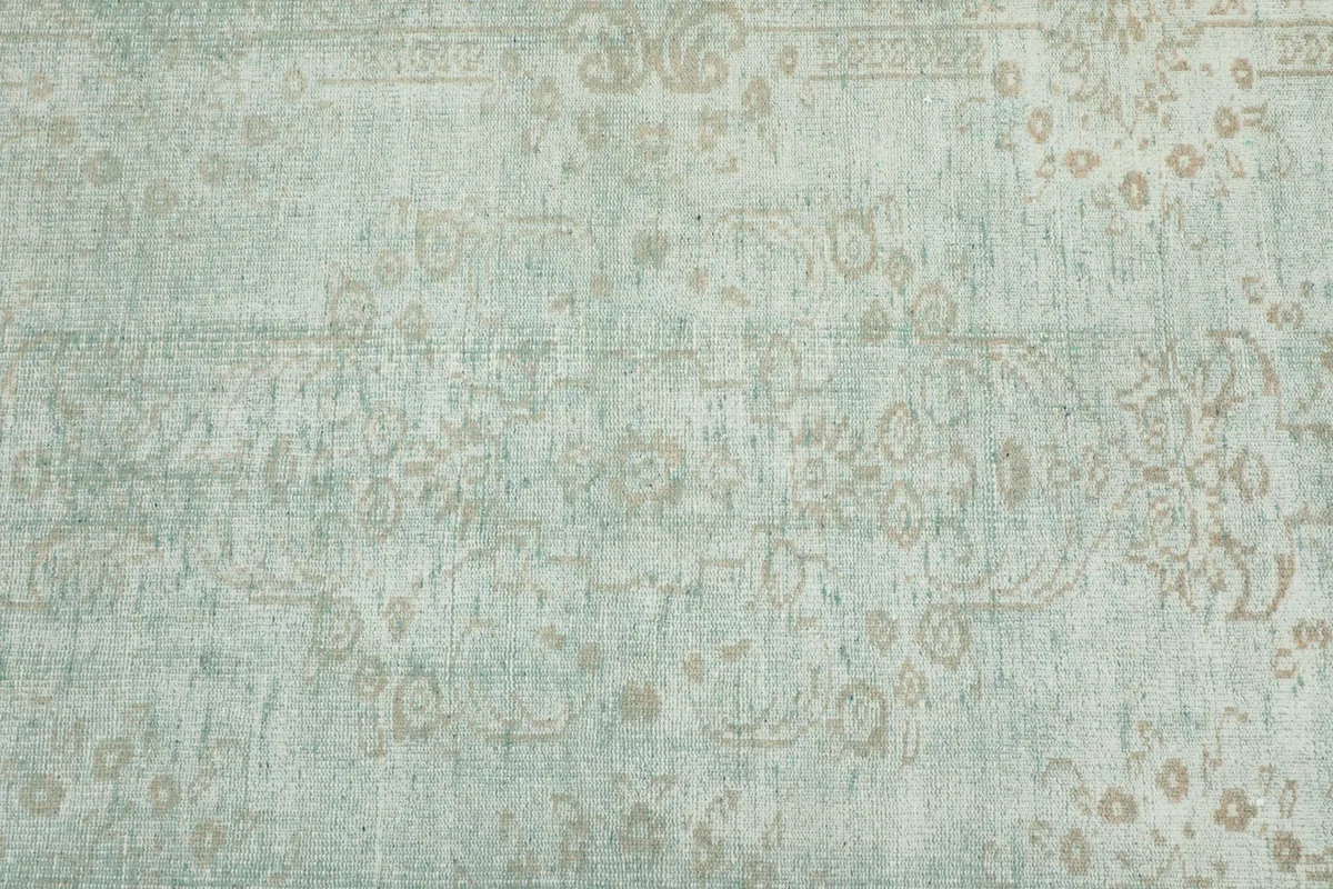 Angled view of the green field and faded beige medallion motif of the hand-knotted rug