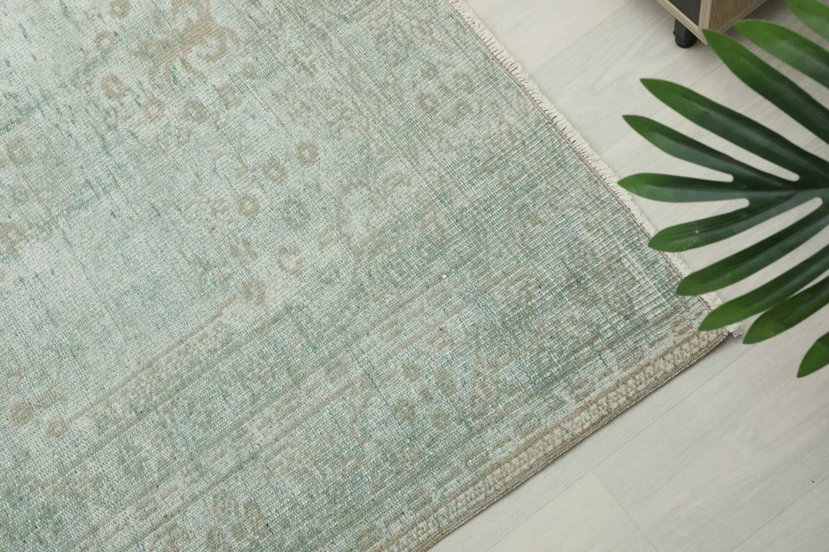 Corner view of the rug on a light floor, showing its subtle green and beige border