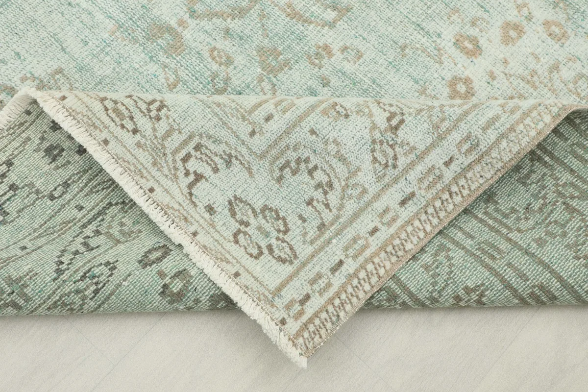 Folded corner of the rug revealing the intricate beige and green border design