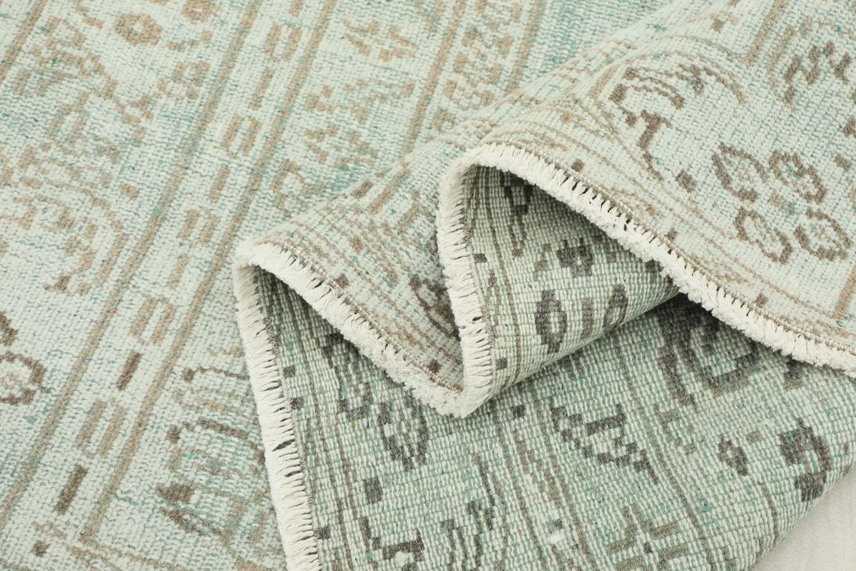 Multiple folds of the rug showing the overall green color and faded patterns