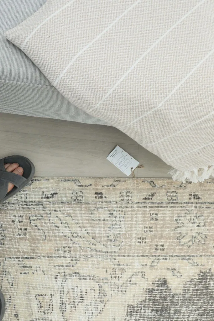 Overhead view of a person's feet on the rug, showing a product tag near a cushion