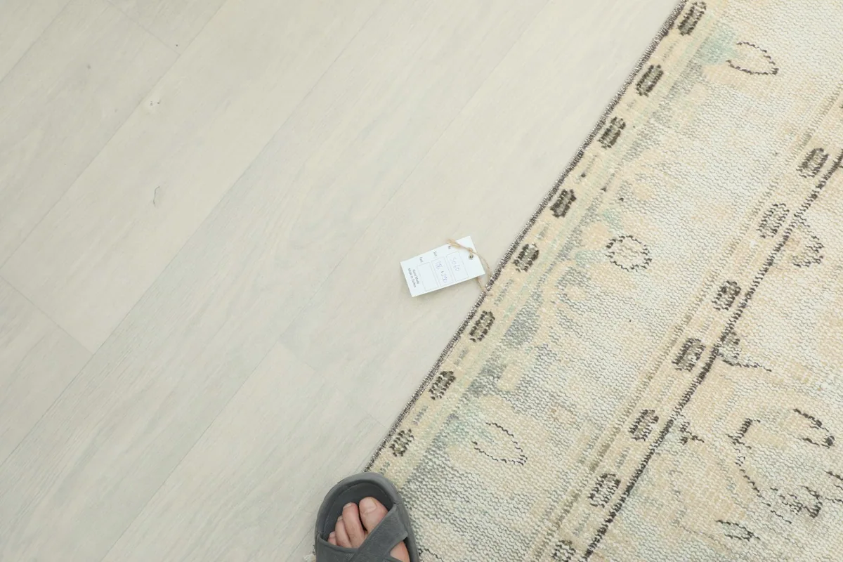 Overhead view showing a foot and a small tag on the light-colored floor next to the rug
