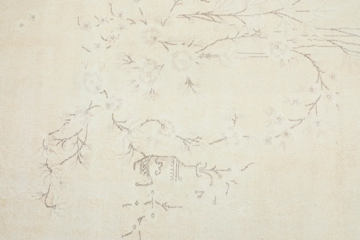 Detail shot showing the faded tan floral and vine patterns on the cream field of the rug.