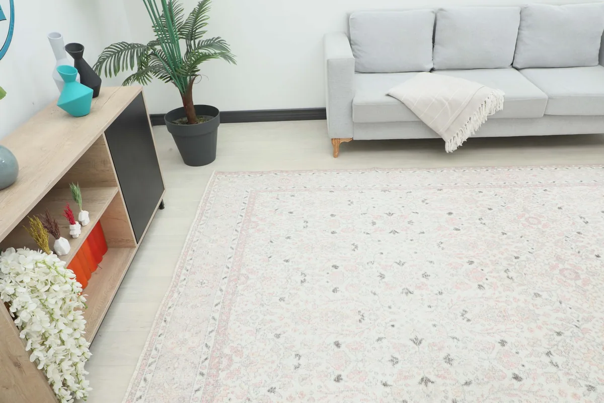 Angle view of the large cream and rose rug in a living space, extending under a light gray sofa.