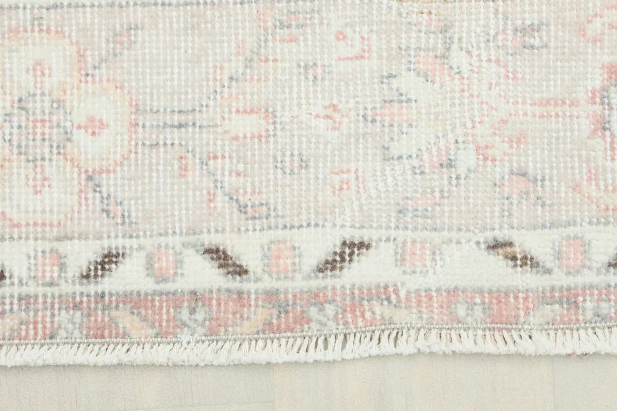 Close-up view of the rug's border showing the subtle rose, gray, and cream geometric patterns.