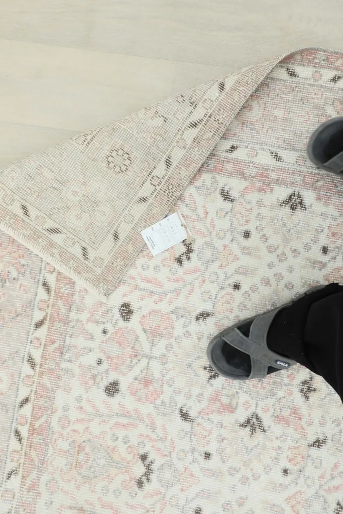 Overhead view with a person's feet and the rug's back, showing the fine knotting and vintage tag.