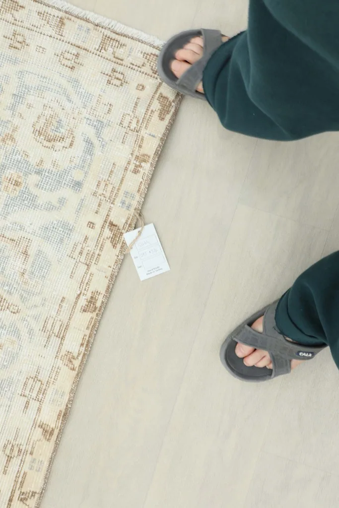 Person's feet standing near the rug, providing a sense of scale and the low pile height.