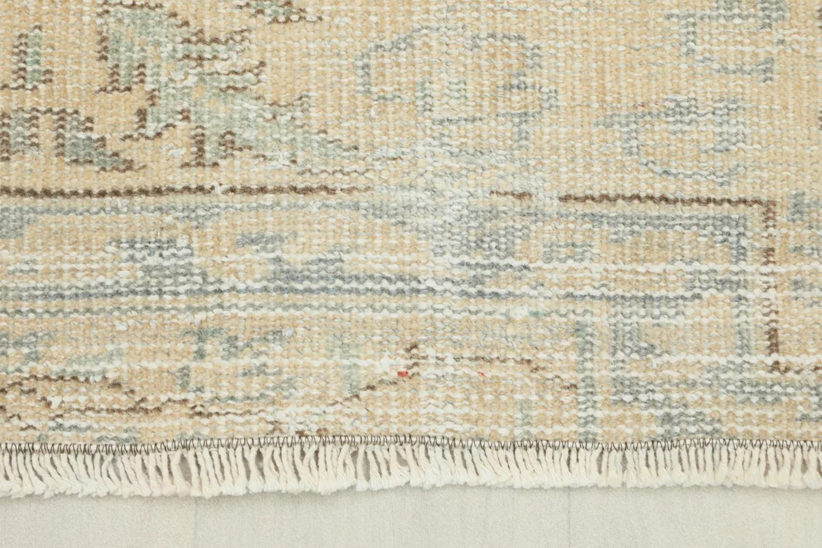 Close-up view of the rug's border and fringe, showing the low wool pile and faded blue gray tones