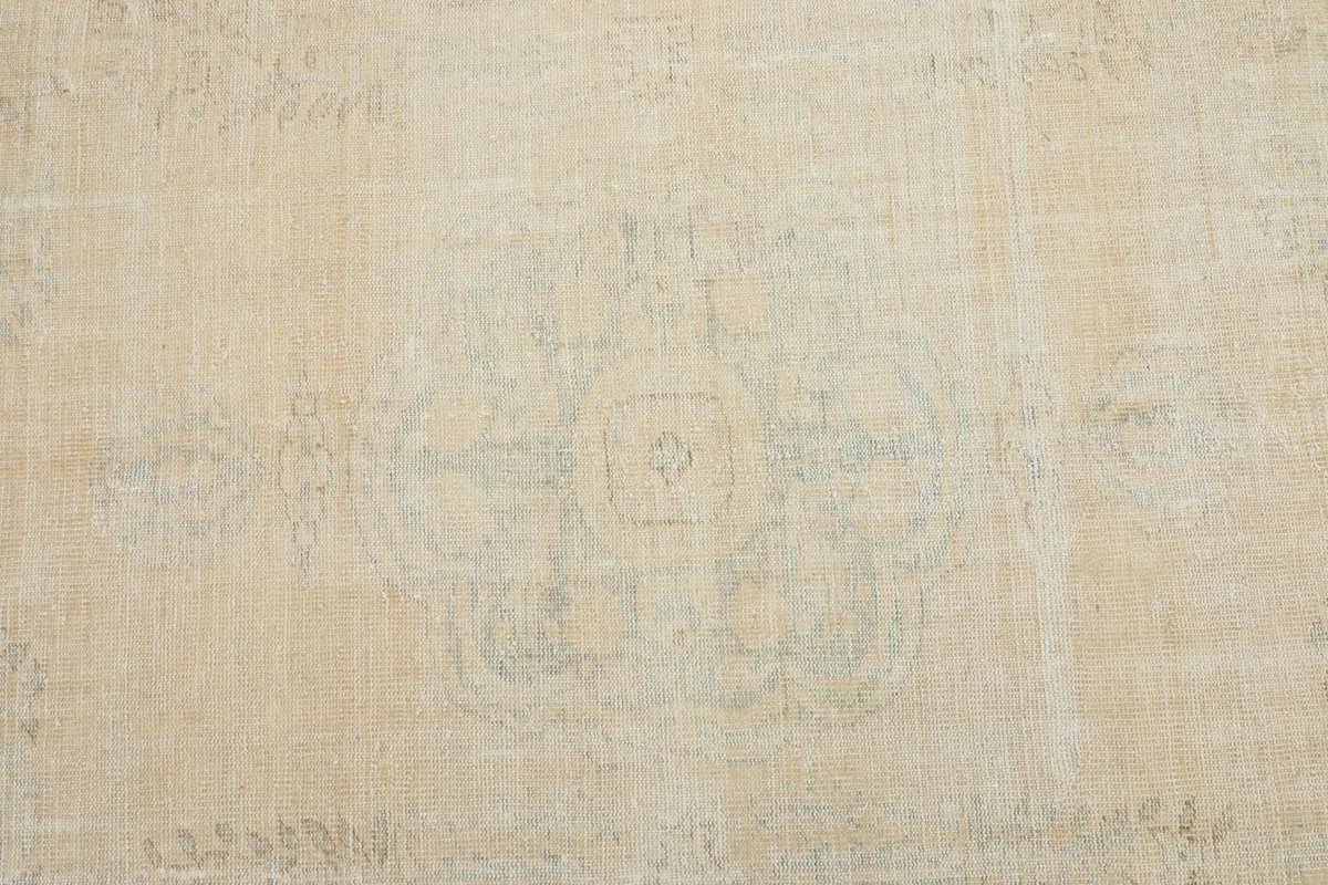 Overhead view of the center of the vintage rug, highlighting the muted beige field and faint medallion motif