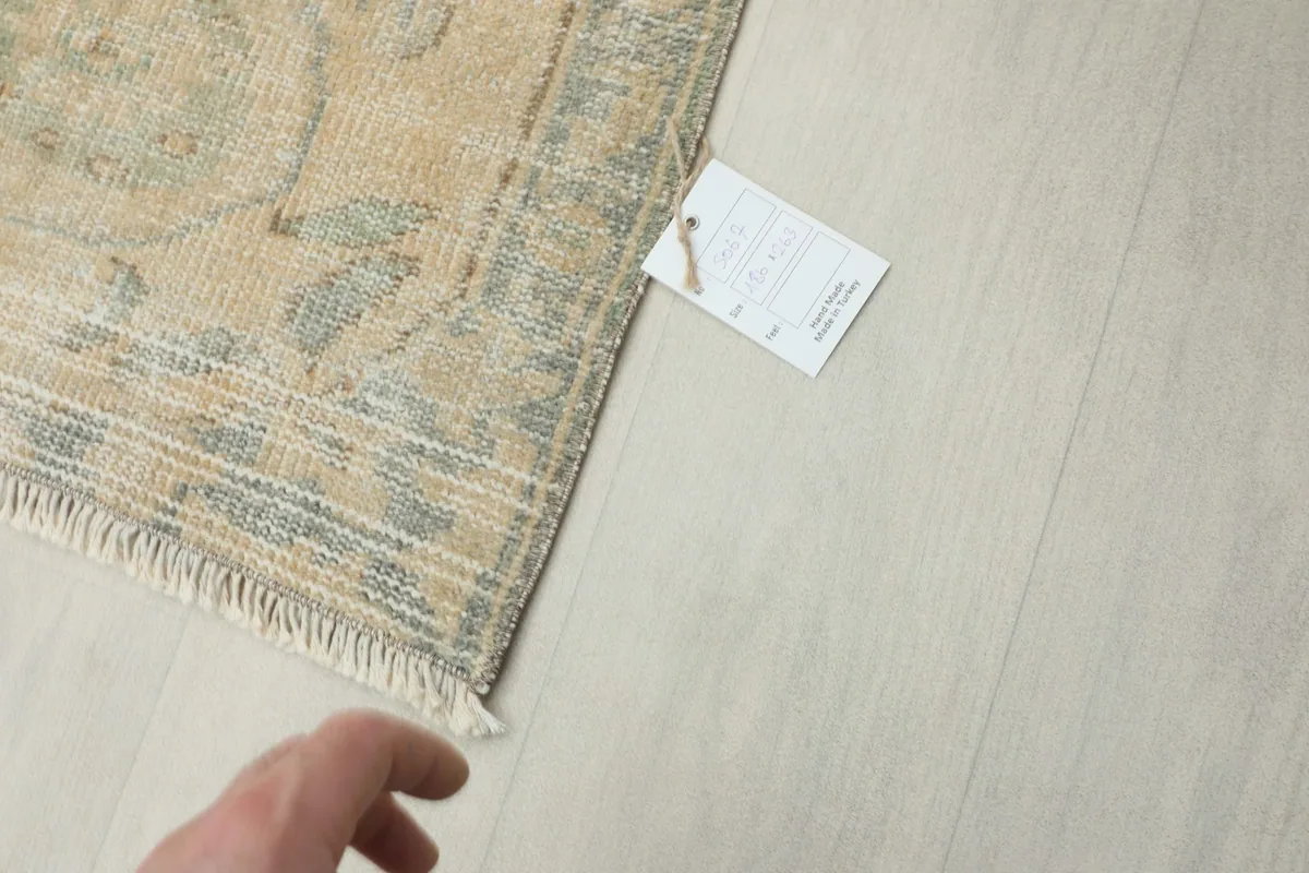 Hand pointing to the care tag on the corner of the rug, indicating professional cleaning