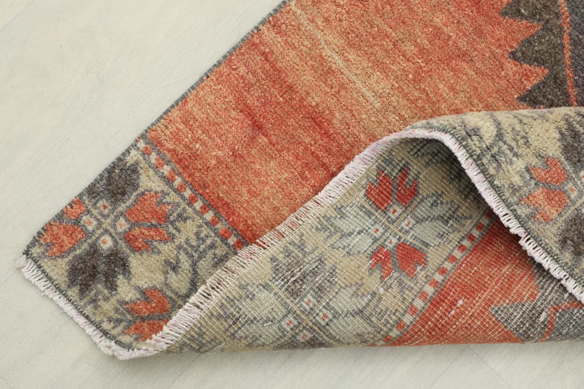 Corner of the rug folded back to reveal the back of the rug and the border design