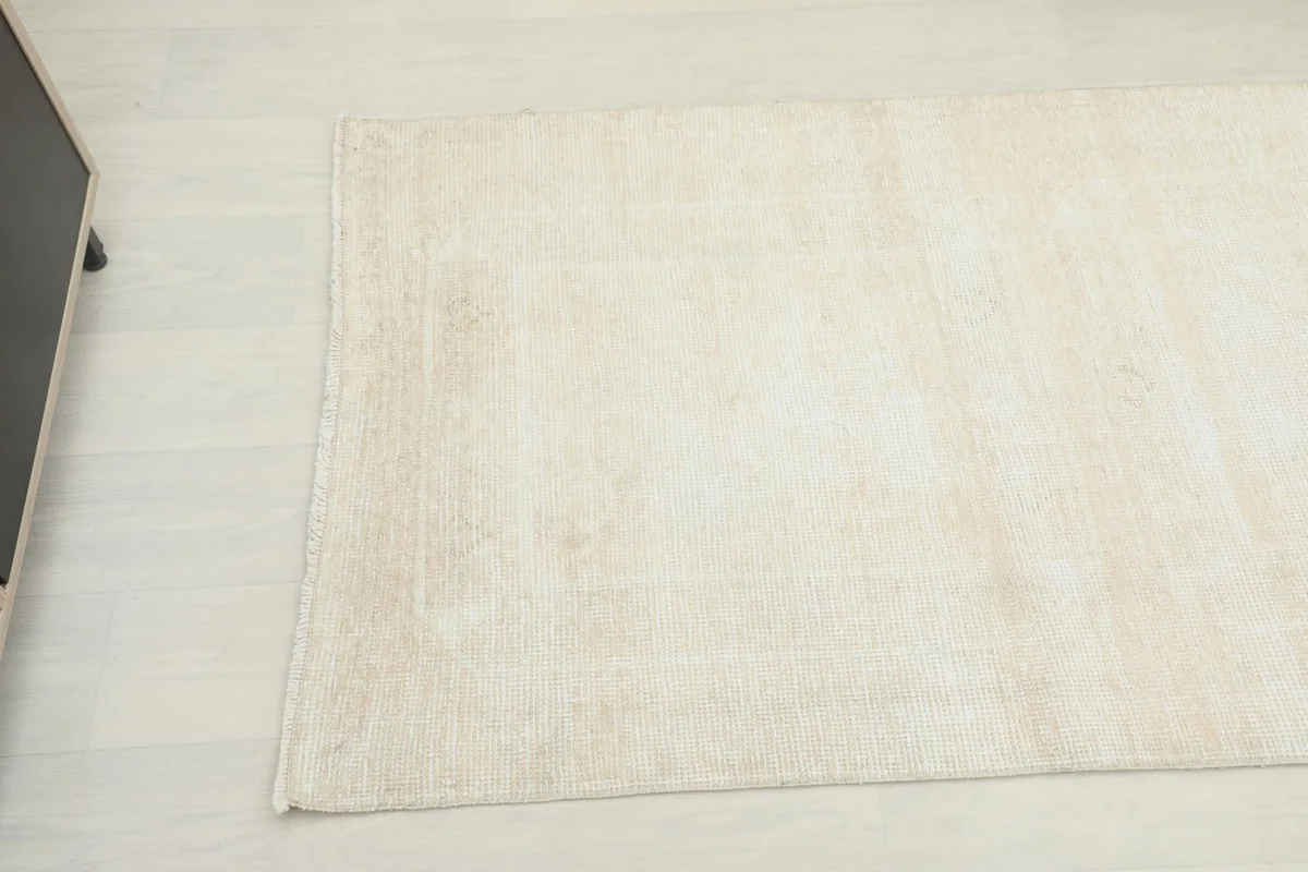 Corner view of the beige runner rug, highlighting its distressed surface and muted tones.