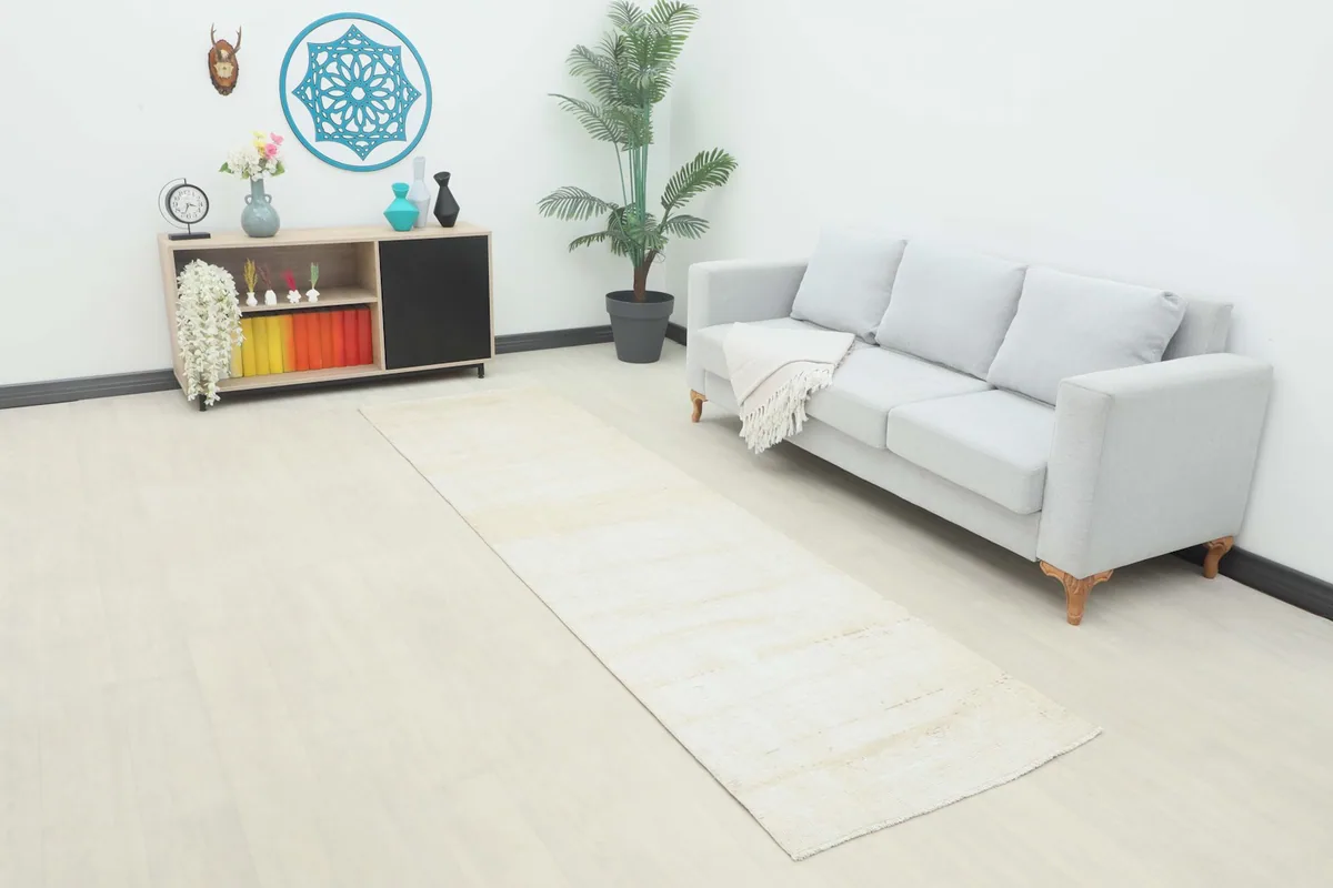 Beige runner rug in a room setting, next to a gray sofa and a small console table.