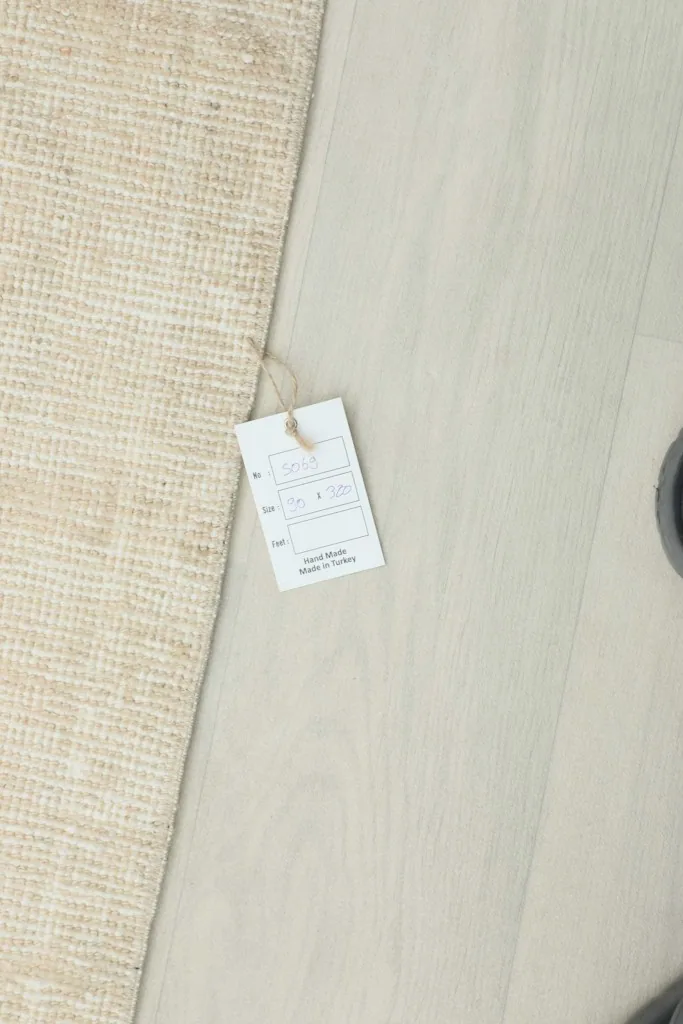 Product tag laid on the floor next to the rug, indicating details like material and origin.