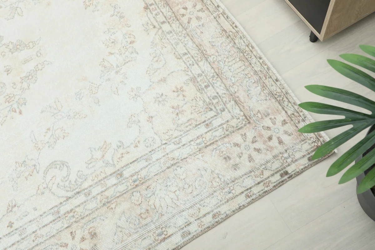 High-angle view showing a corner of the rug with its intricate border design and the overall ivory and beige palette.