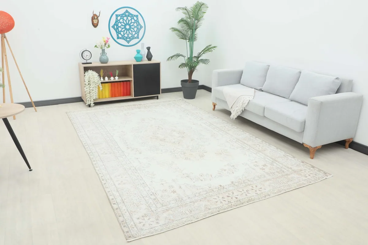 The ivory and beige vintage Anatolian rug displayed in a bright room with a light gray sofa and modern decor.