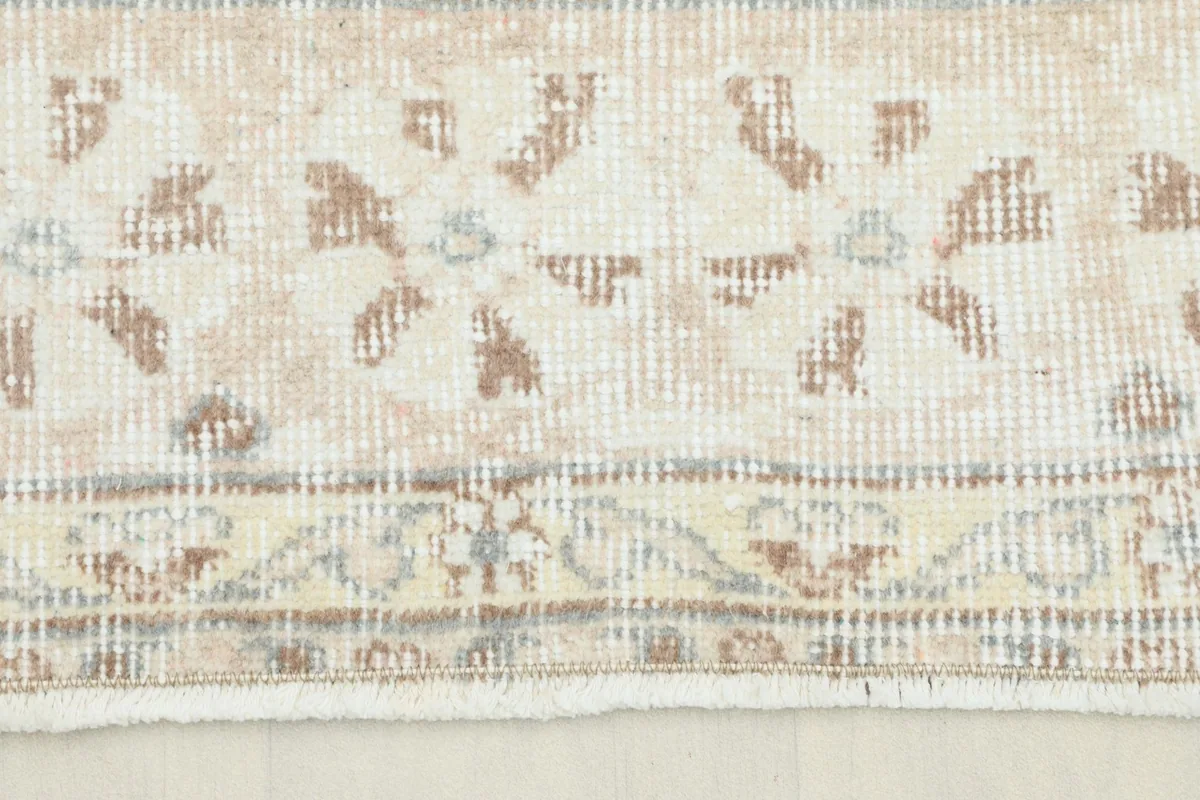 Close-up detail of the rug's border showing faded beige and blue floral patterns and the subtle fringe.