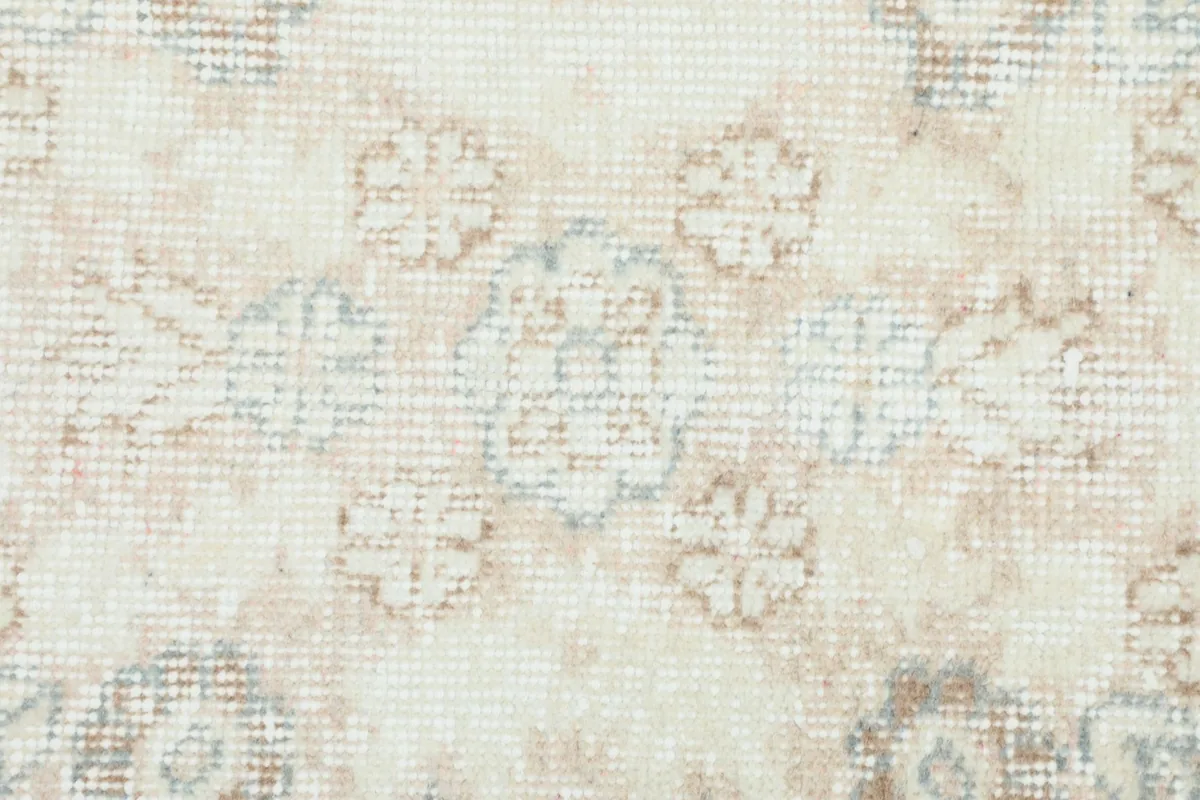 Macro detail of the hand-knotted wool pile, showing the texture and muted floral patterns in beige and blue.